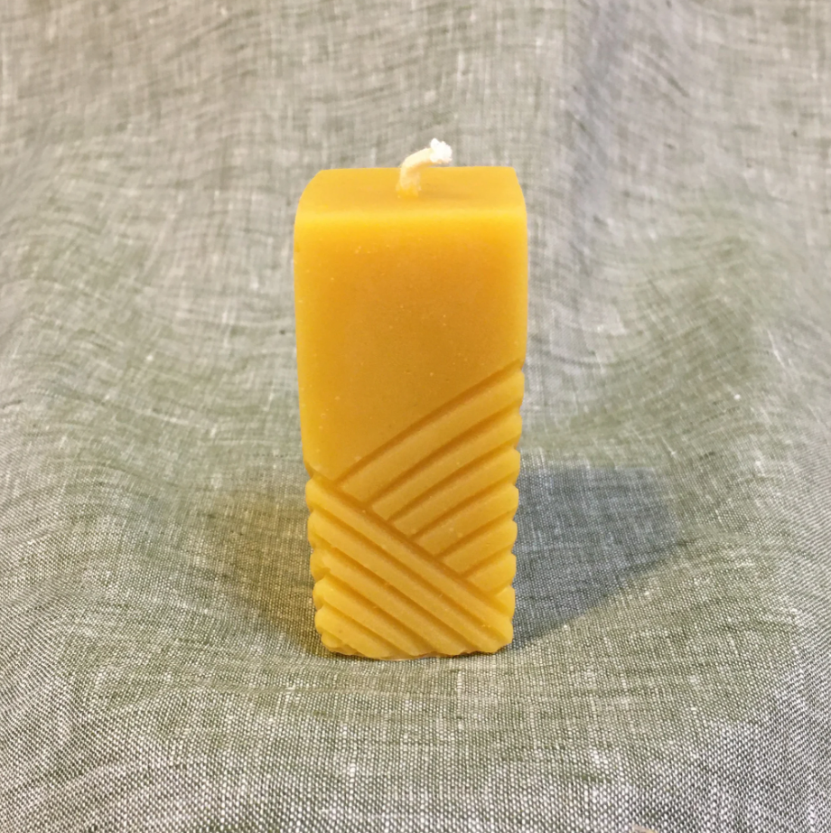 Picture of a tall rectangle yellow beeswax candle on a linen background